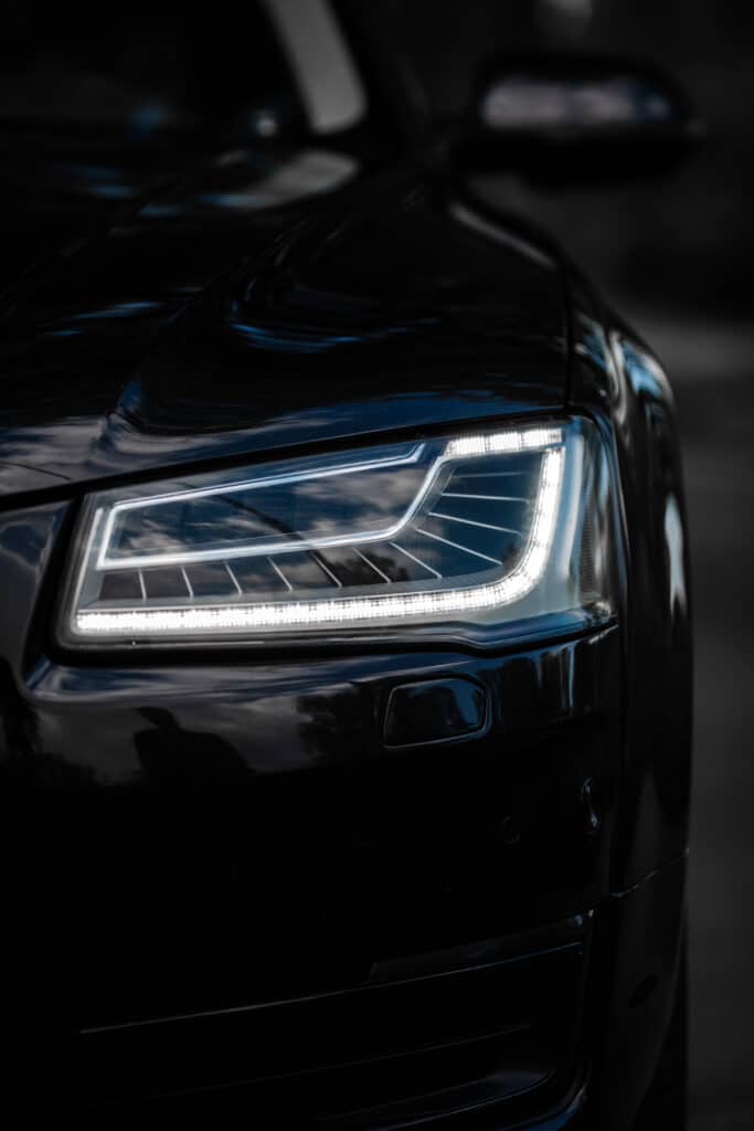 Phare LED de Voiture Noire Luxueuse en Gros Plan Gros plan sur le phare LED allumé d'une voiture noire brillante, reflets subtils de nuages sur la carrosserie.