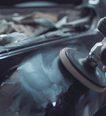 Polissage intensif d'une carrosserie sombre avec une polisseuse orbitale, laissant des traces circulaires sur la peinture.